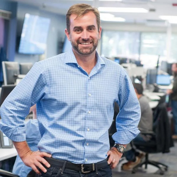 Jon Russell, CIO, in a blue shirt standing confidently in an office environment.