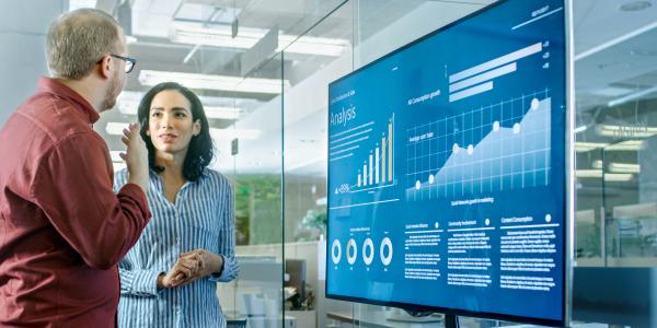 two people in talking in front of a large monitor