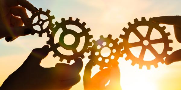 four hands holding gear pieces with the sun as background