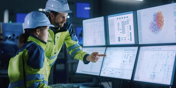 Two helmeted workers looking at computer screens