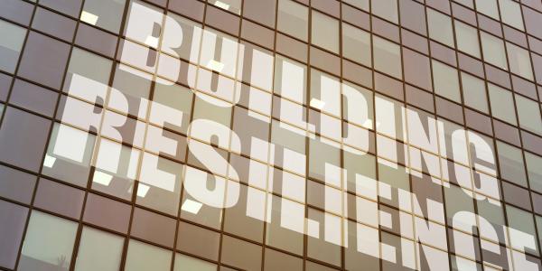 Image of a modern building facade with the words "BUILDING RESILIENCE" reflected on its glass surface.