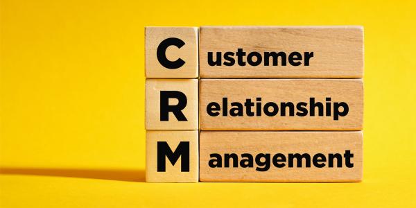 Image of wooden blocks stacked to spell "CRM Customer Relationship Management" on a bright yellow background.