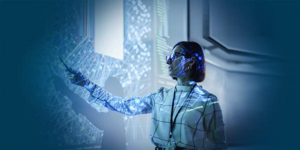 A presenter in a dark room pointing at a large screen displaying complex data visualizations.