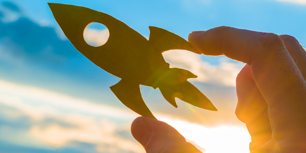 Hand holding a cutout of a rocket against the sky, symbolizing launch and new beginnings.