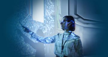 A presenter in a dark room pointing at a large screen displaying complex data visualizations.