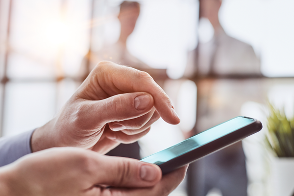Close-up of a person using a smartphone with two blurred figures in the background.